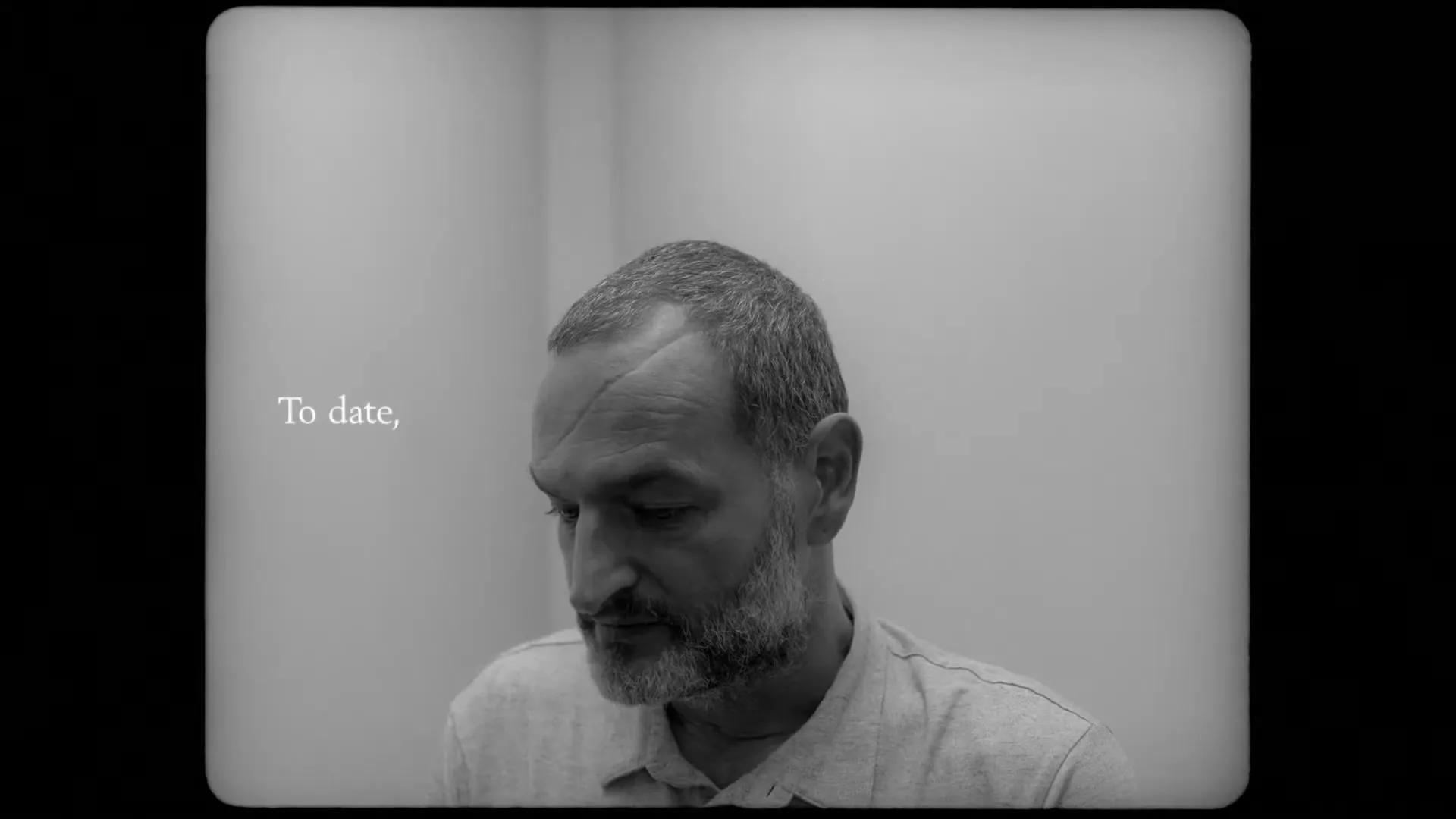 A middle-aged man with a scar on his forehead looks down, then touches his head, in a stark, minimalist room.