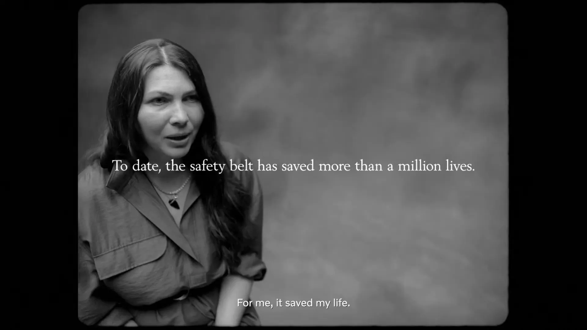A woman with long dark hair and a collared shirt looks to the side and speaks, with text on screen, in a studio.