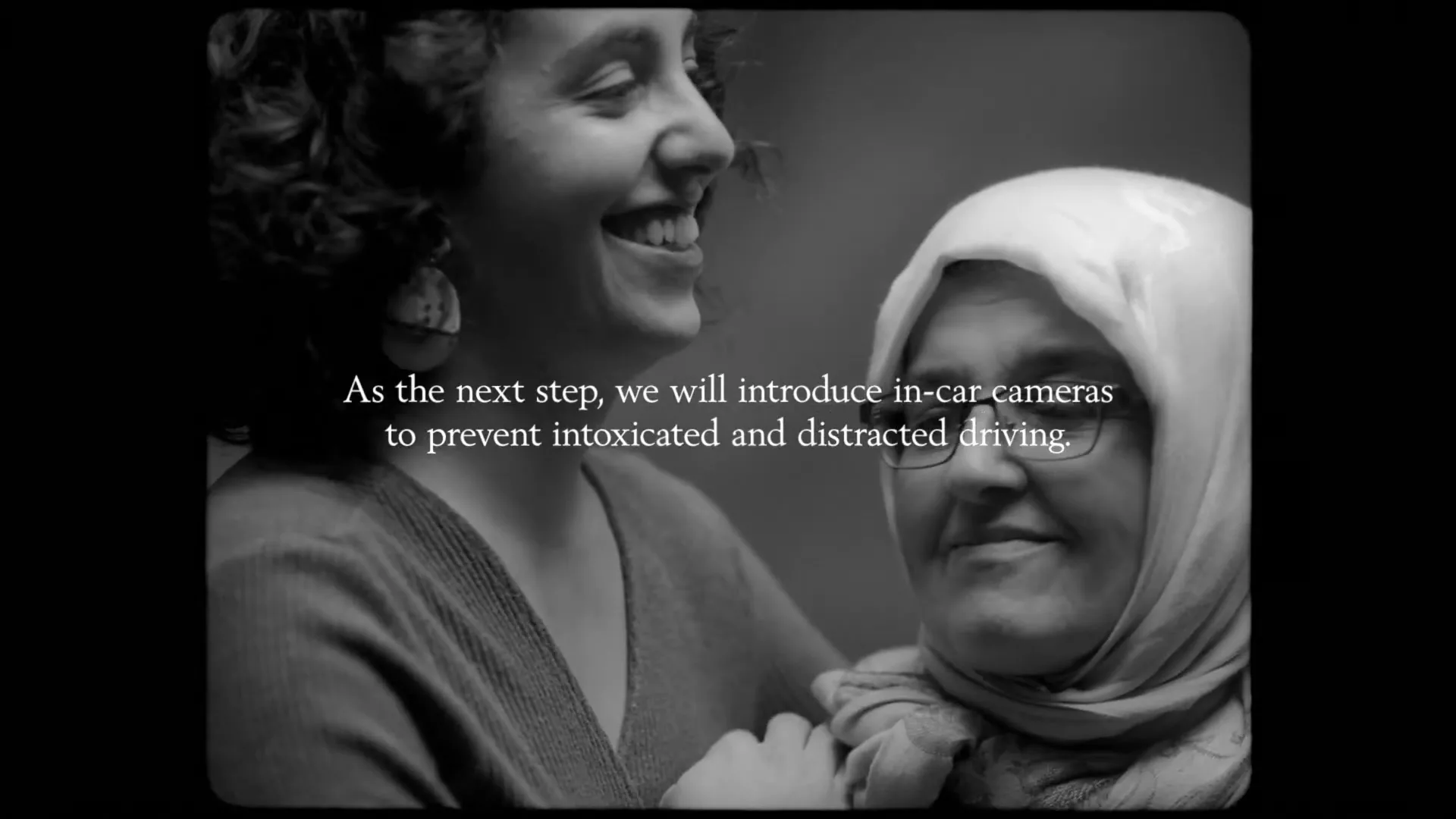 A diverse group of people, including a child, a young woman, and an older woman in a hijab, are shown in black and white, smiling and looking at the camera.