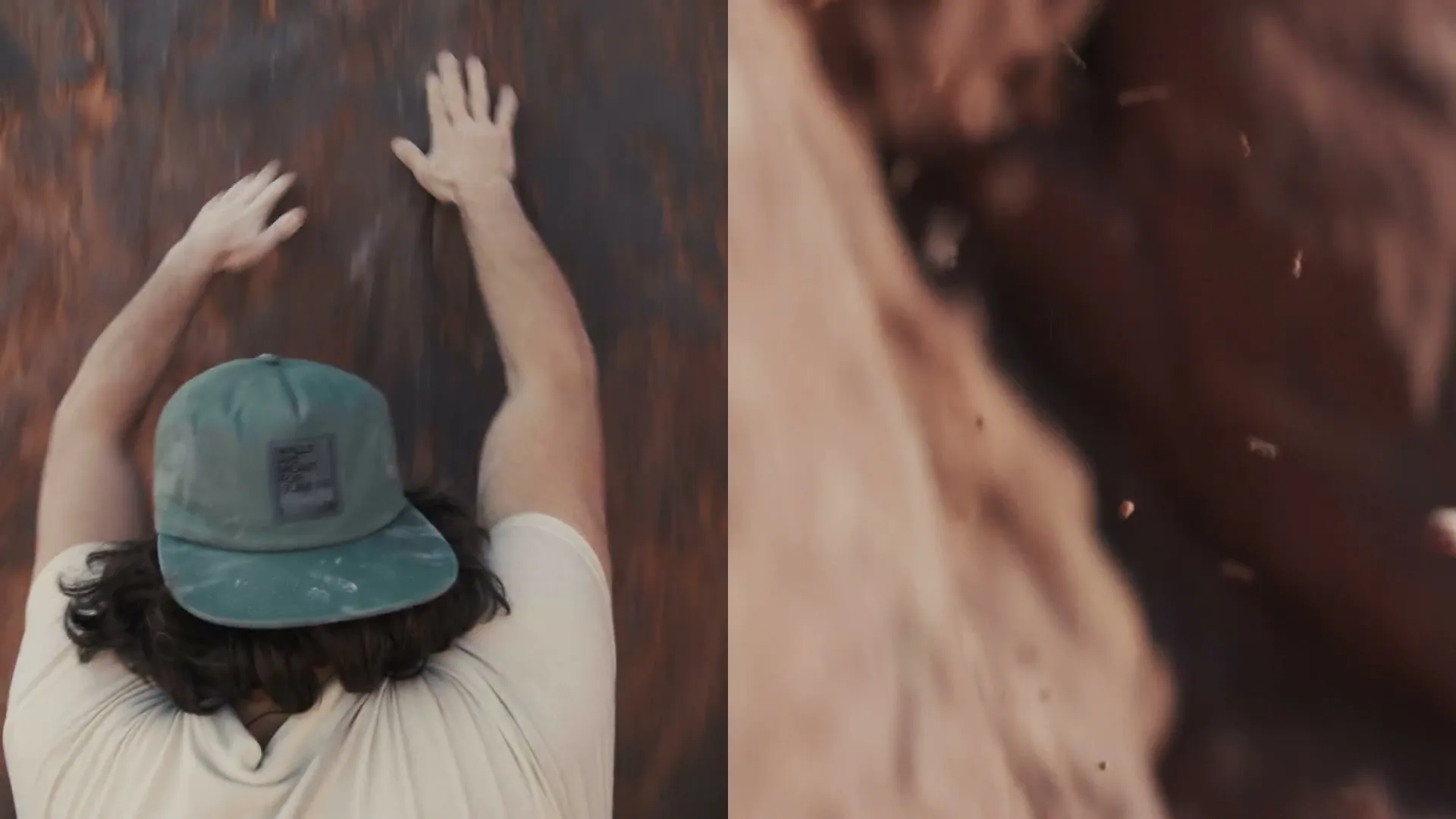 A male rock climber in a green cap and beige shirt is seen from above, climbing a reddish-brown rock face outdoors.