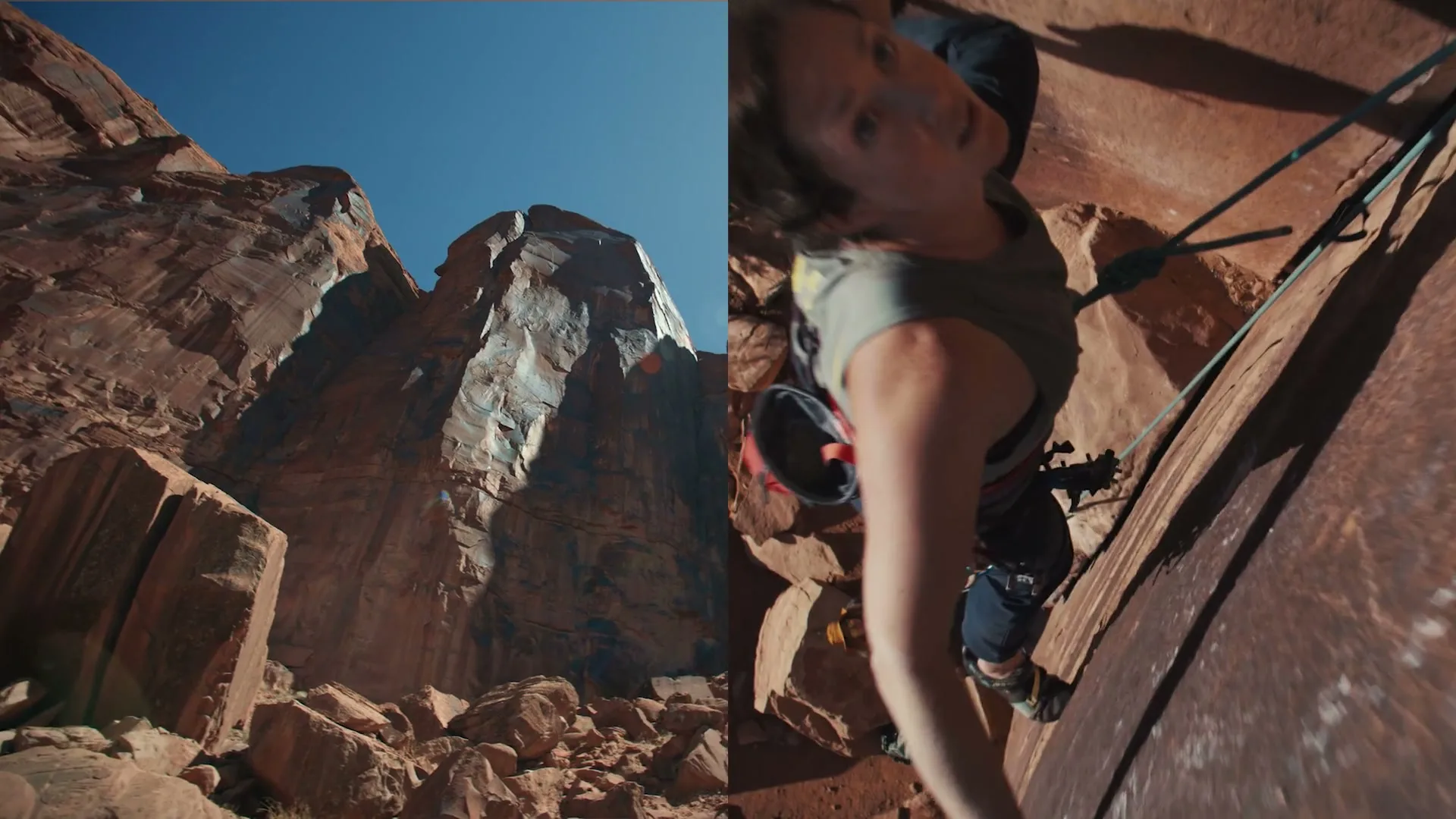 A female rock climber in a grey top and black pants ascends a steep, reddish-brown rock face, with a wide shot of the desert mountains beside her.