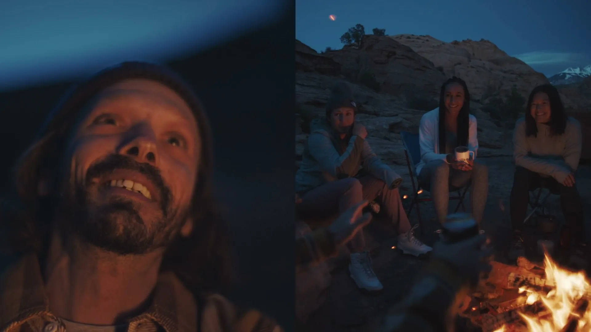 A man with a beard and beanie looks up, smiling, while three women sit around a campfire at night in a desert landscape.