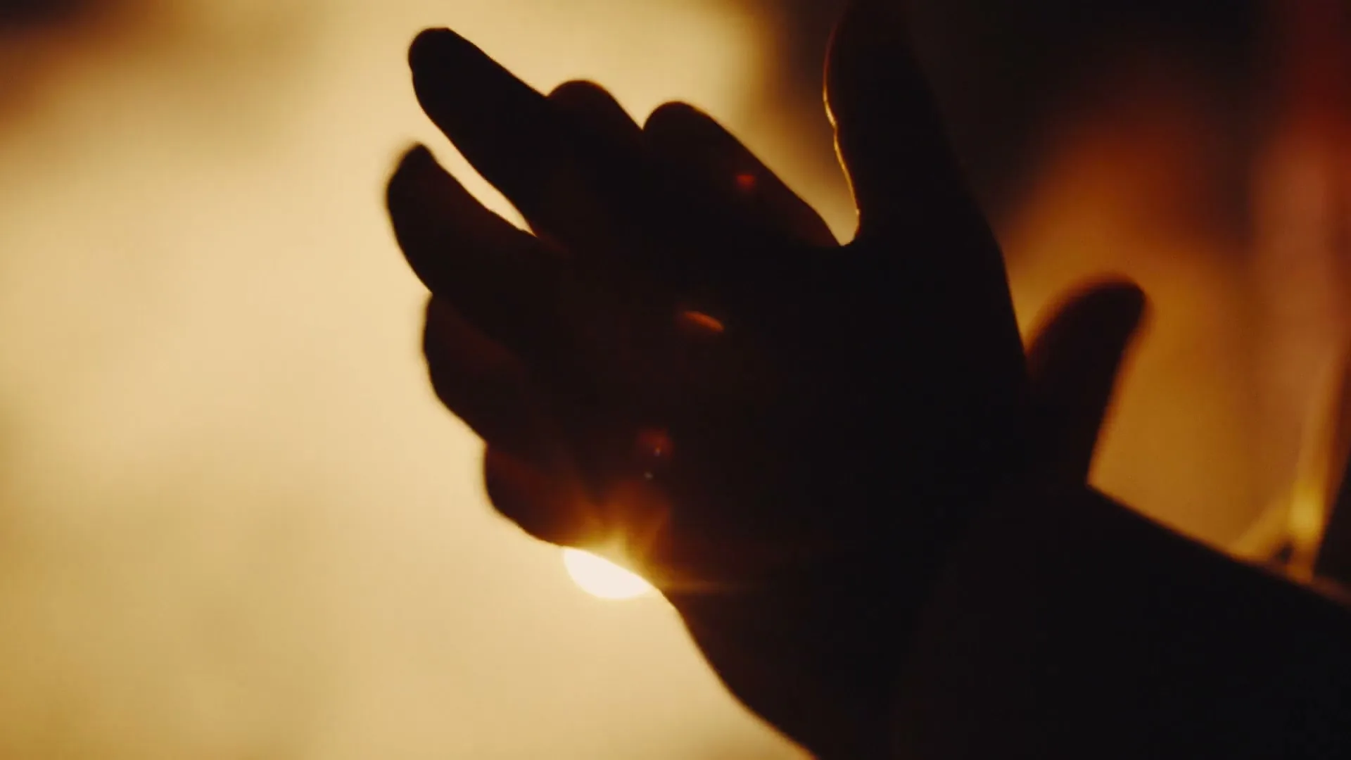 A silhouetted hand claps against a bright, warm background, creating a lens flare effect.