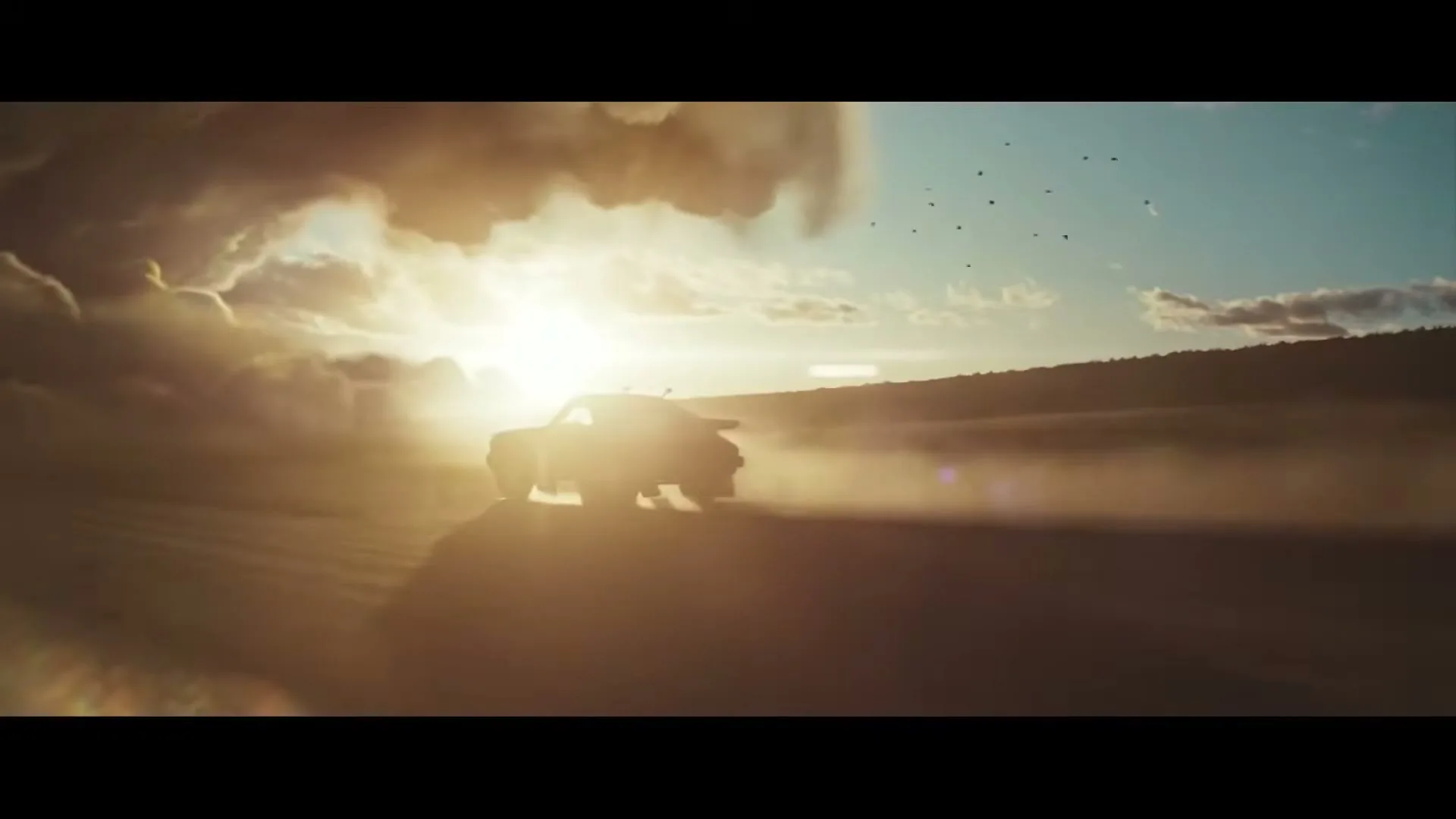 A Porsche 911 Dakar drives across a dusty desert landscape, silhouetted against a bright golden sunset with dramatic clouds.