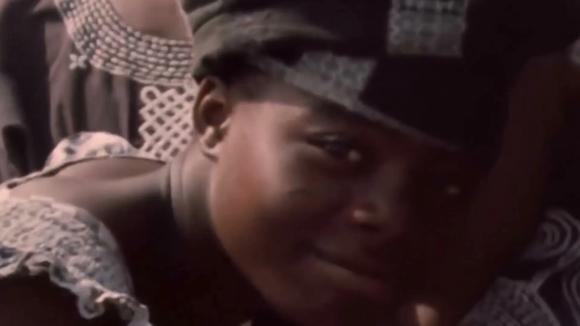 A young person in traditional attire smiles at the camera, with a bright lens flare appearing at the end of the shot.