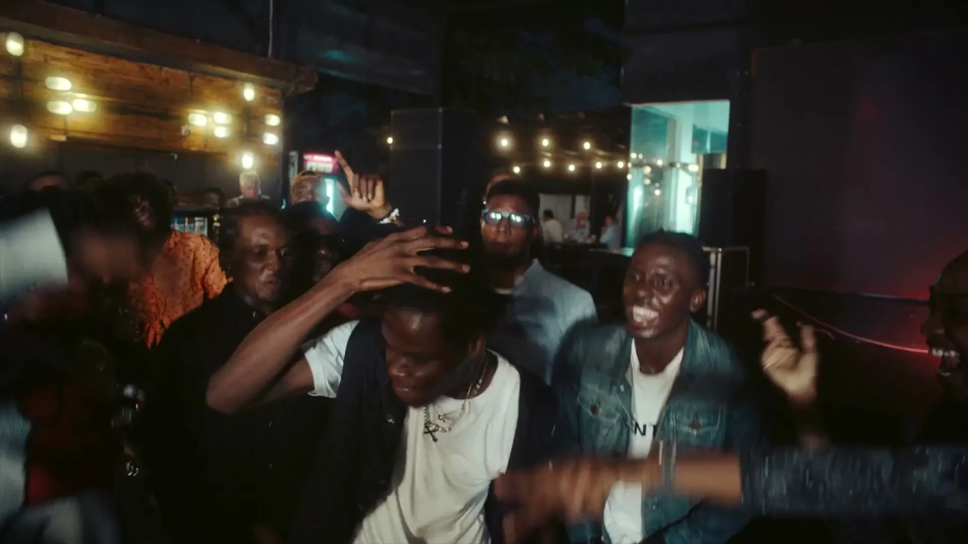 A group of young adults dance energetically in a dimly lit club, celebrating and having fun together.
