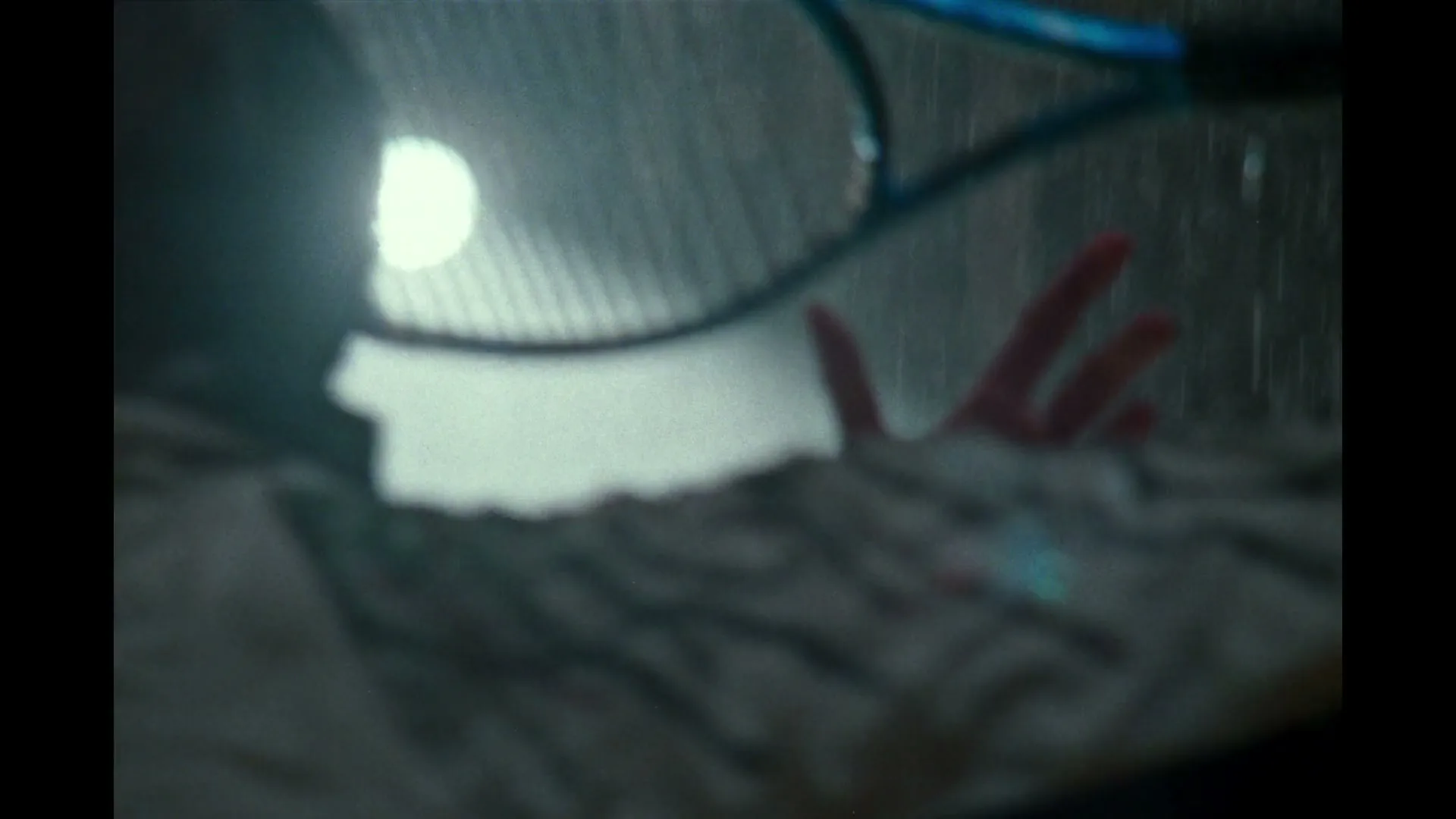 A blurry shot of a person's back and shoulder, with a tennis racket and a bright light source in the background, as if playing in the rain.