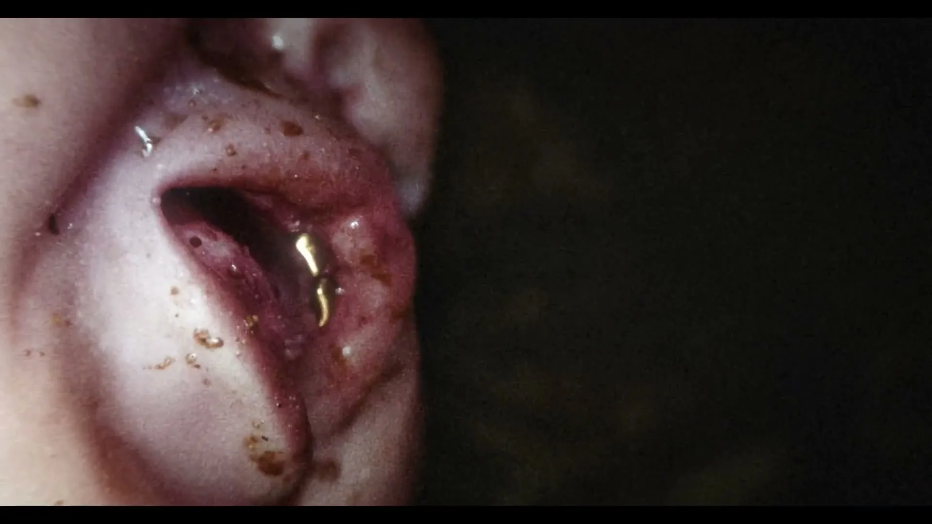 A very close-up shot of a human ear, covered in dirt and what appears to be blood, with a golden sprout growing out of it.