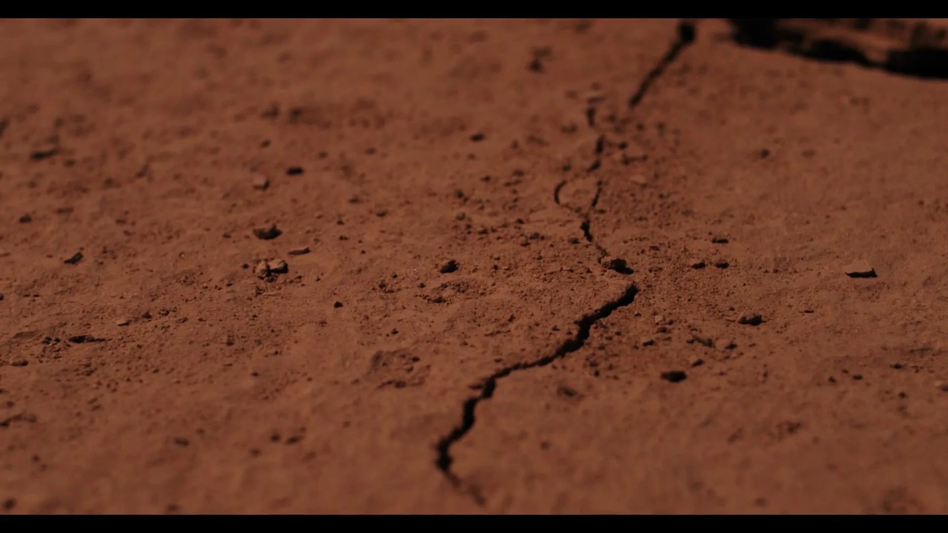 A close-up shot of dry, cracked earth, with the cracks slowly expanding and deepening, revealing more texture.