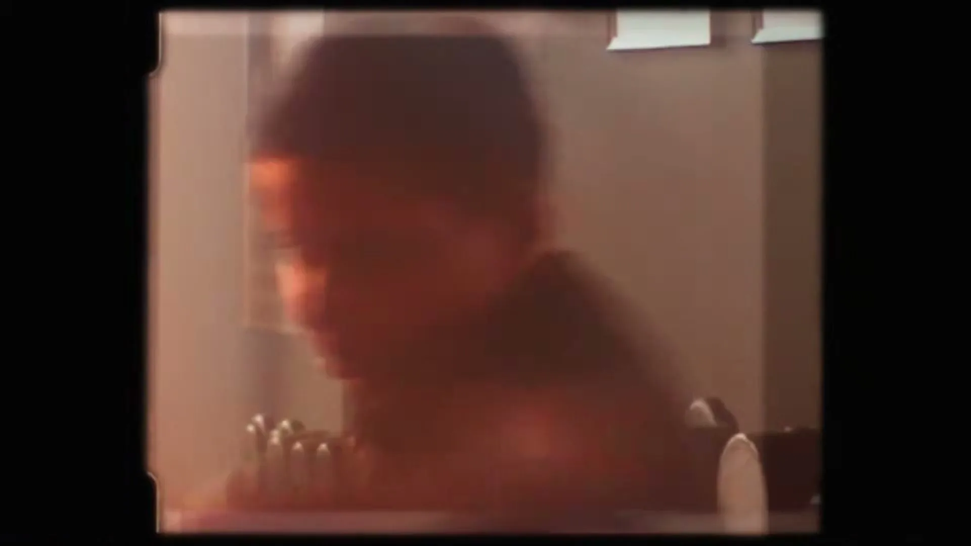 A blurry shot of a young male boxer with dark hair, wearing a dark top, training with weights in an interior setting.