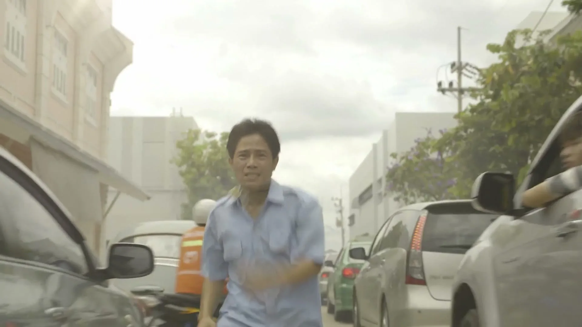 A man in a light blue shirt runs frantically through a busy street, surrounded by cars, looking distressed.