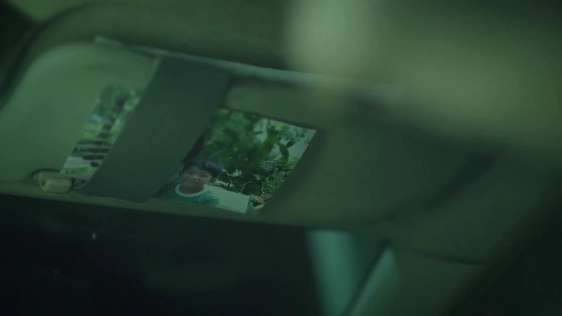 A photo of a smiling young boy is tucked into a car's sun visor, which is then flipped up.