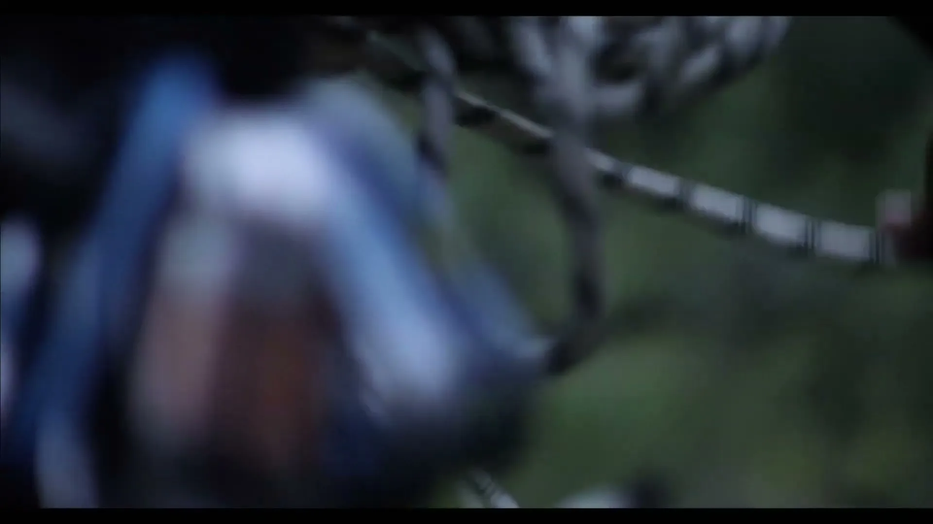 A person's hand is seen in a medium closeup, pulling a climbing rope through a carabiner, with a blurred natural background.