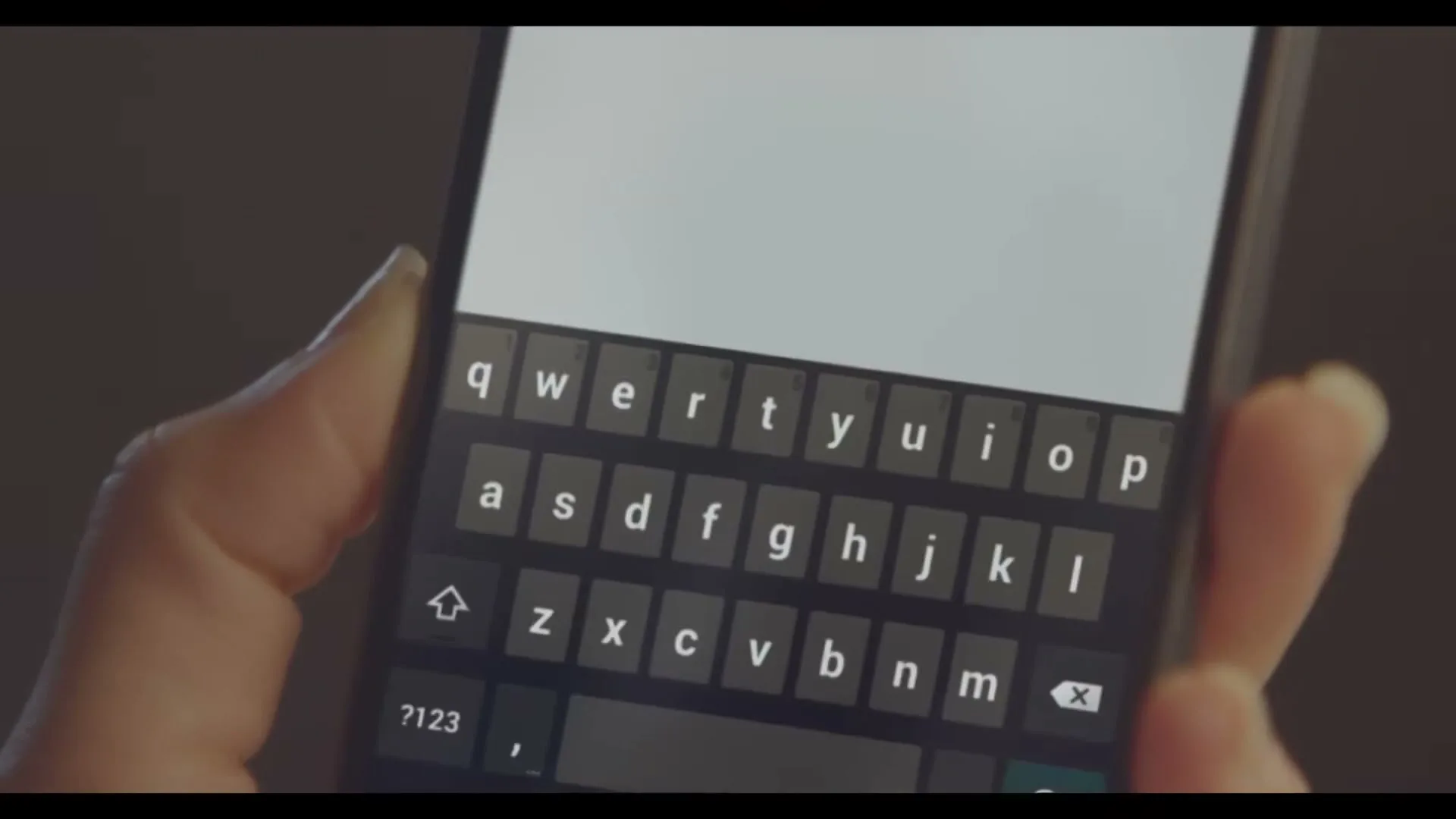 A person's hand holds a smartphone, with the screen displaying a virtual keyboard, in an interior setting.