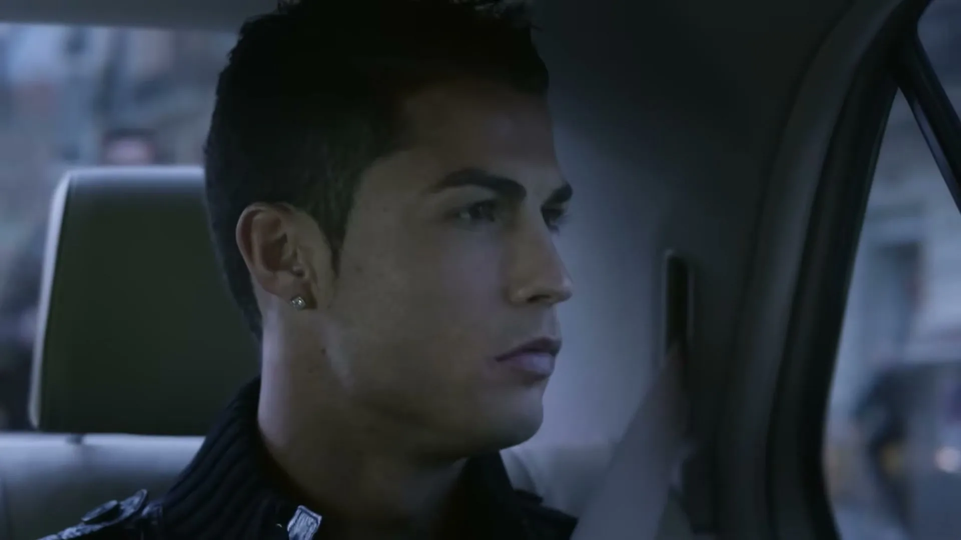 Cristiano Ronaldo, a male in his 20s, sits in the back of a car, looking out the window with a neutral expression.