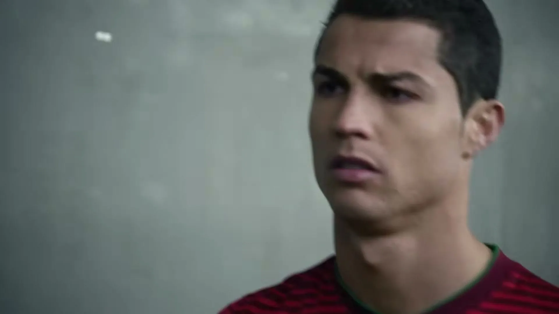 Cristiano Ronaldo, a male soccer player in his 20s, looks concerned while wearing a red and green soccer jersey in an interior setting.