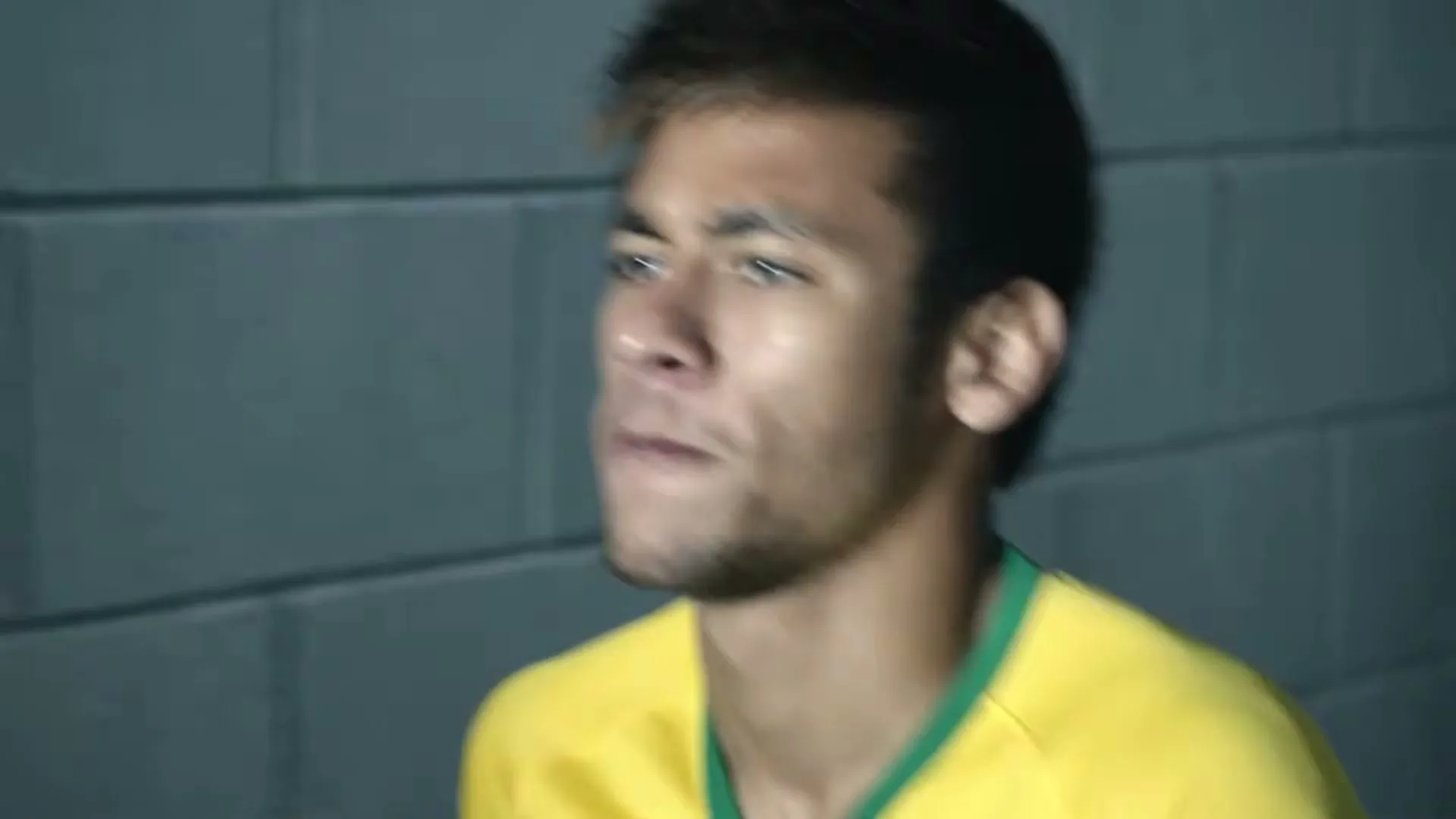A young male soccer player in a yellow jersey looks determined, standing in a locker room.