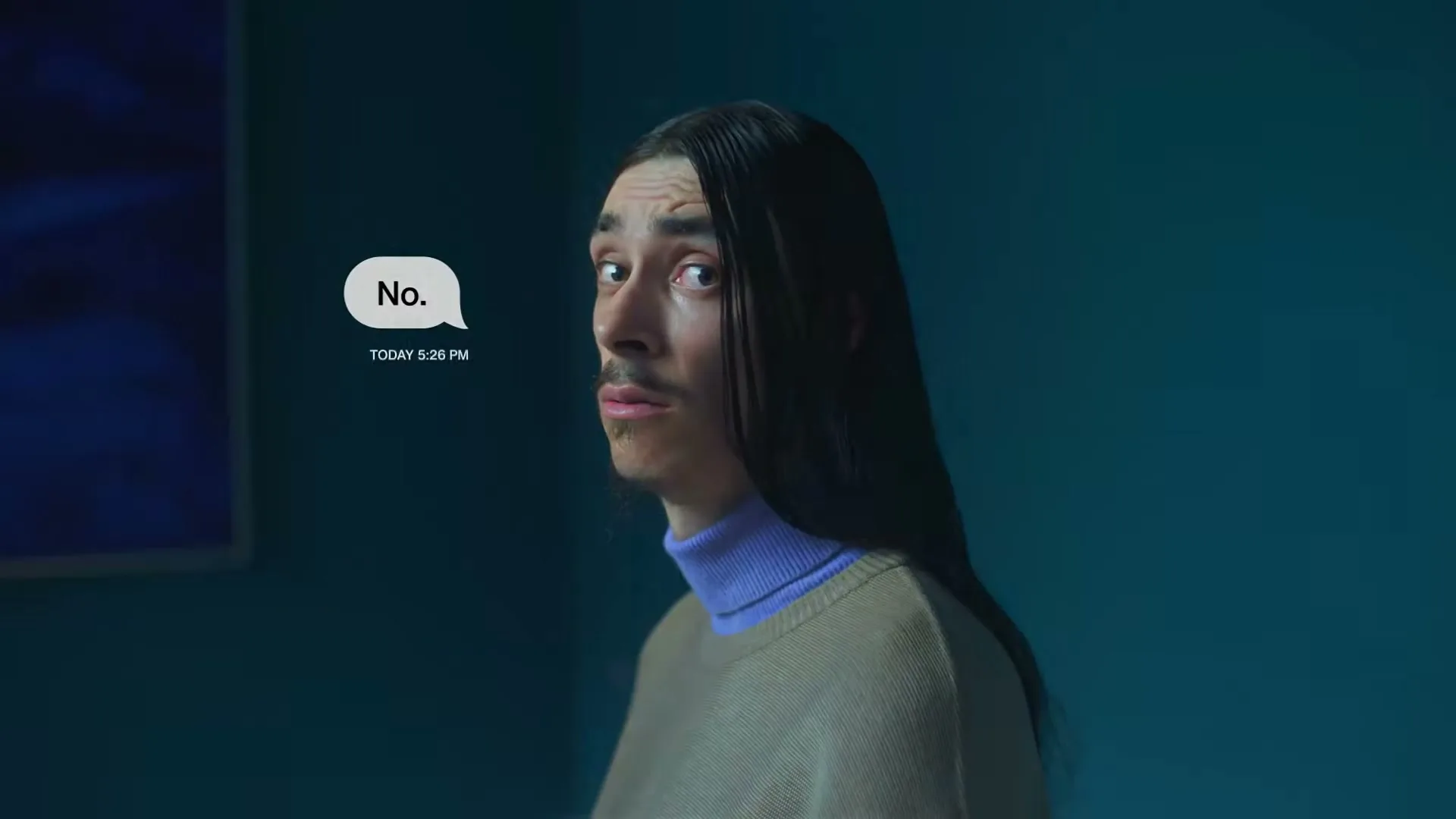 A man with long dark hair and a mustache looks over his shoulder at the camera, with a text bubble saying "No." next to him, in a blue room.