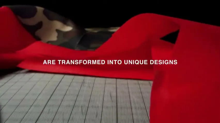 A red fabric ribbon unfurls and twists over a dark wooden surface, revealing a camouflage pattern underneath, with text overlay.