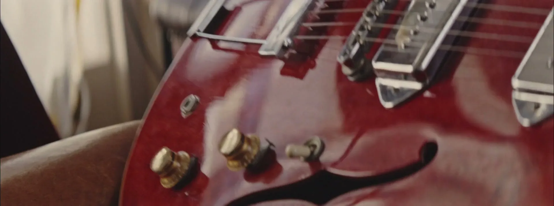 A person's dark-skinned hand adjusts a knob on a shiny red electric guitar, with strings and pickups visible.