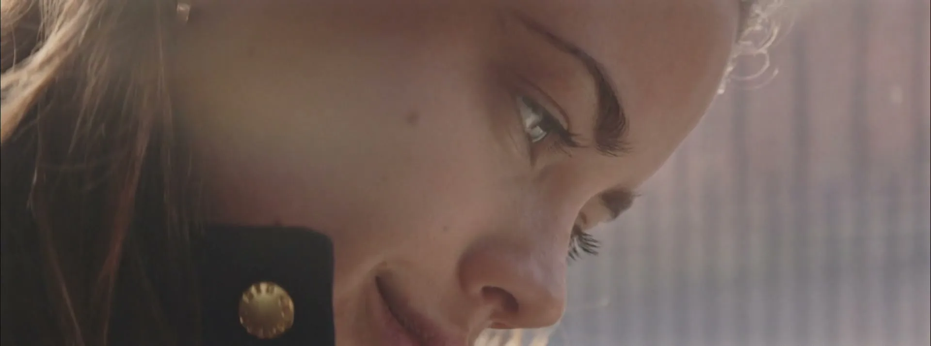 A young woman with light brown hair and a subtle smile looks down, with a reflection of light on her face.