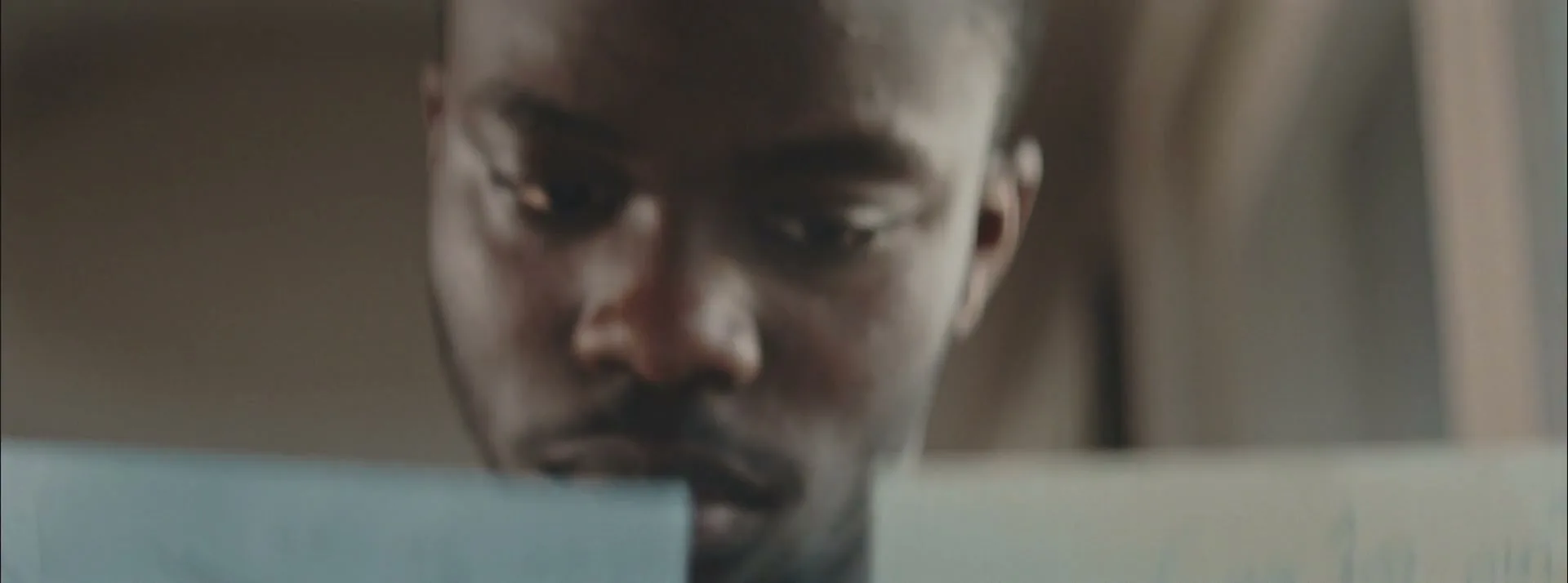 A young Black man with a beard looks down intently at papers, his face partially obscured by them.
