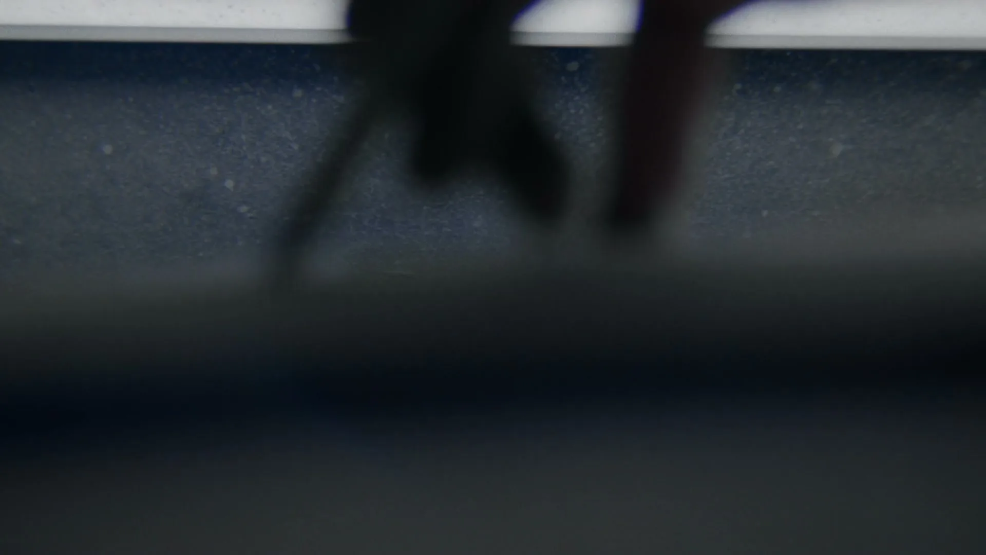 A blurry, out-of-focus shot of a person's hands and a surfboard fin, suggesting movement and action.