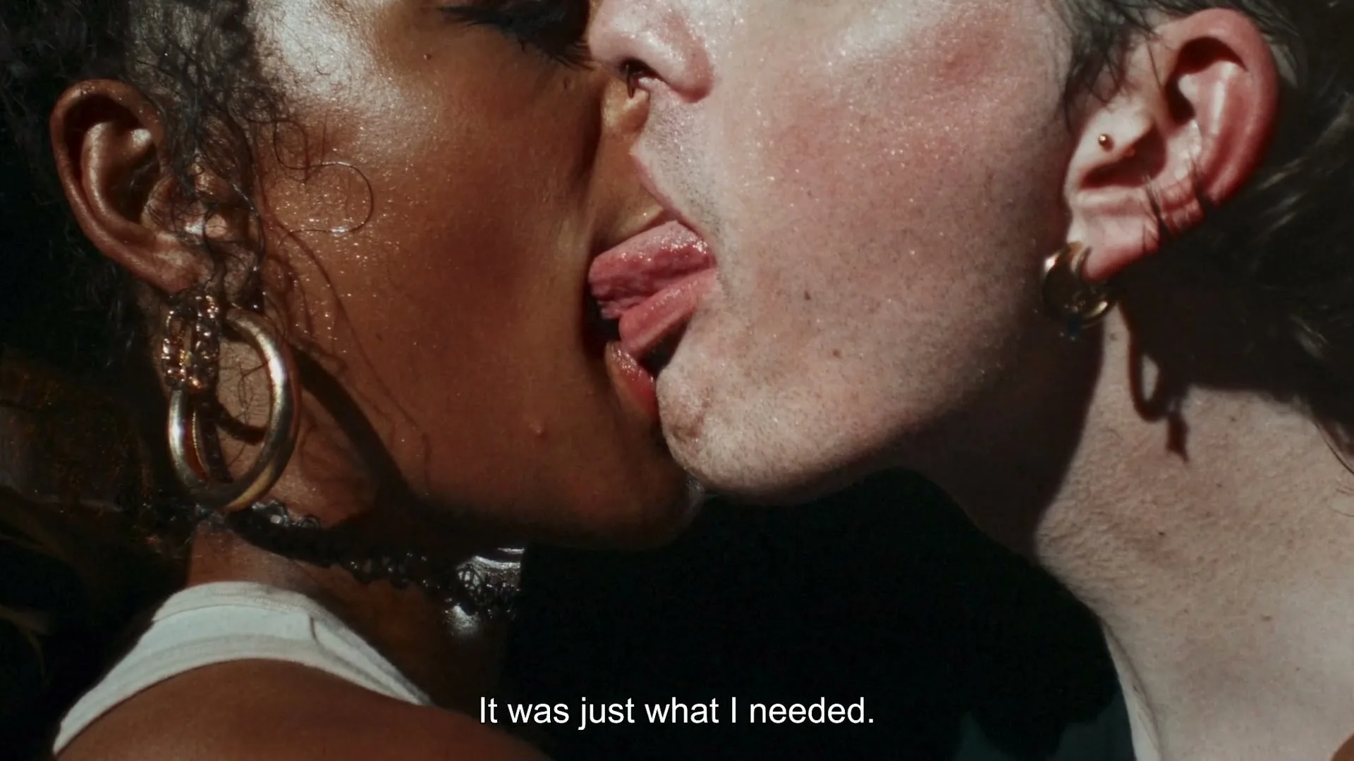 A diverse couple passionately French kisses, their tongues intertwined, in a dark, crowded club, with sweat glistening on their skin.