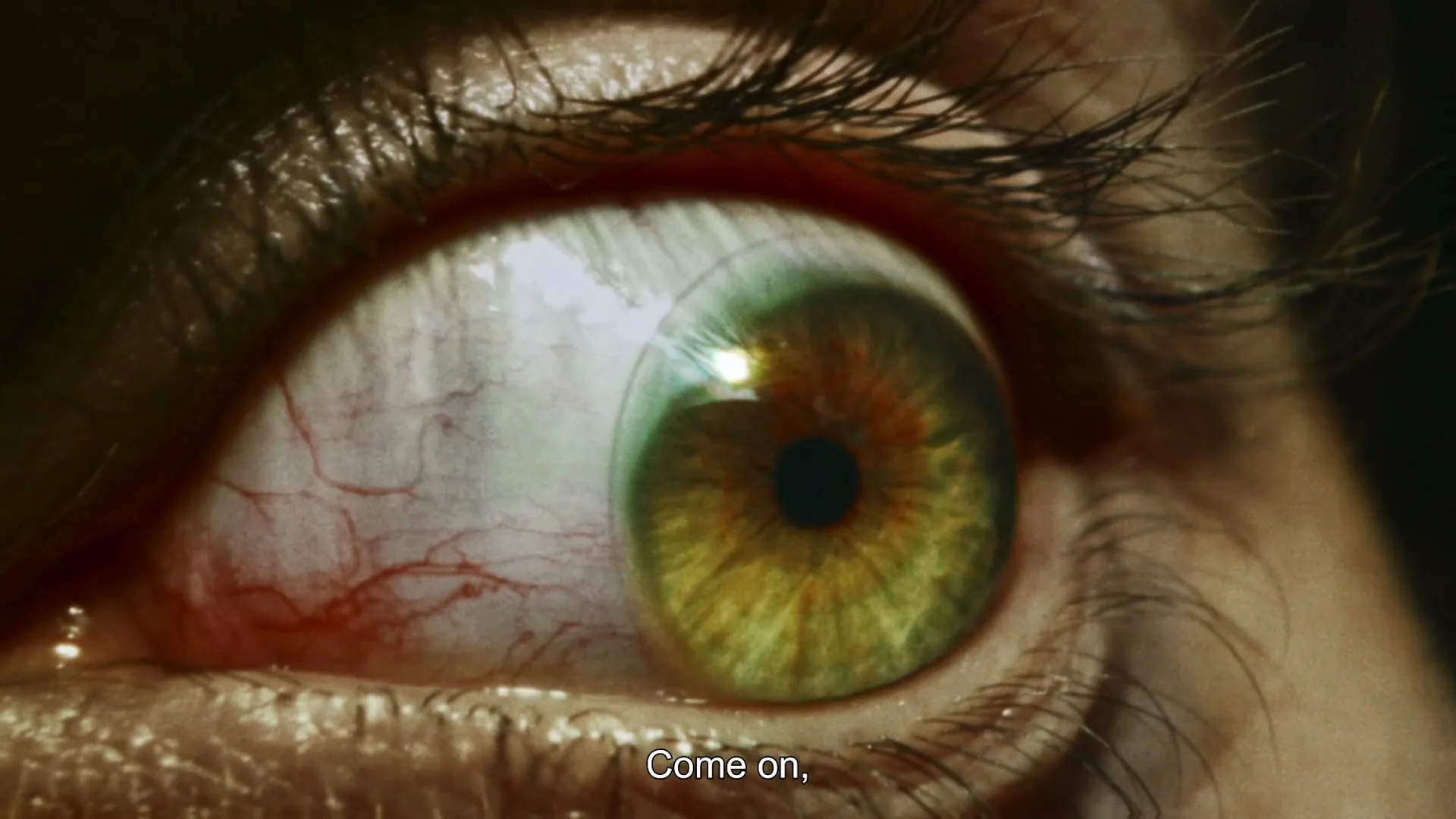 A close-up shot of a person's green eye, bloodshot and wide open, with the pupil dilating and contracting, as on-screen text appears.