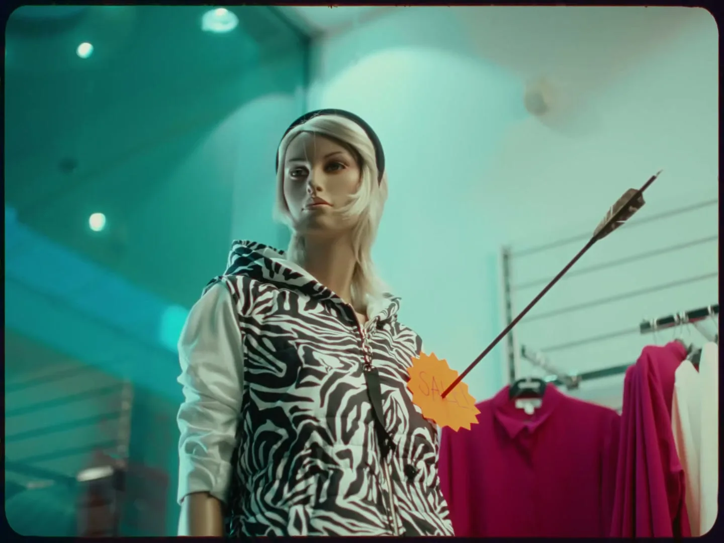A female mannequin with blonde hair and a zebra print hoodie has an arrow with a "SALE" tag stuck in its chest, in a brightly lit clothing store.