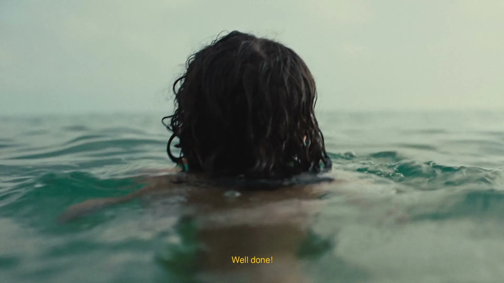 A person with dark, wet hair is seen from behind, swimming in the ocean with text on screen.