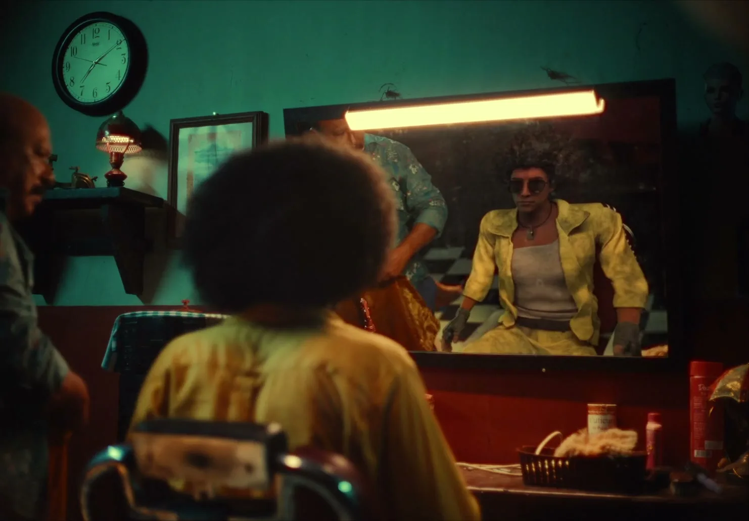 A person with an afro sits in a barber's chair, looking into a mirror where a barber is reflected, in a dimly lit barbershop.