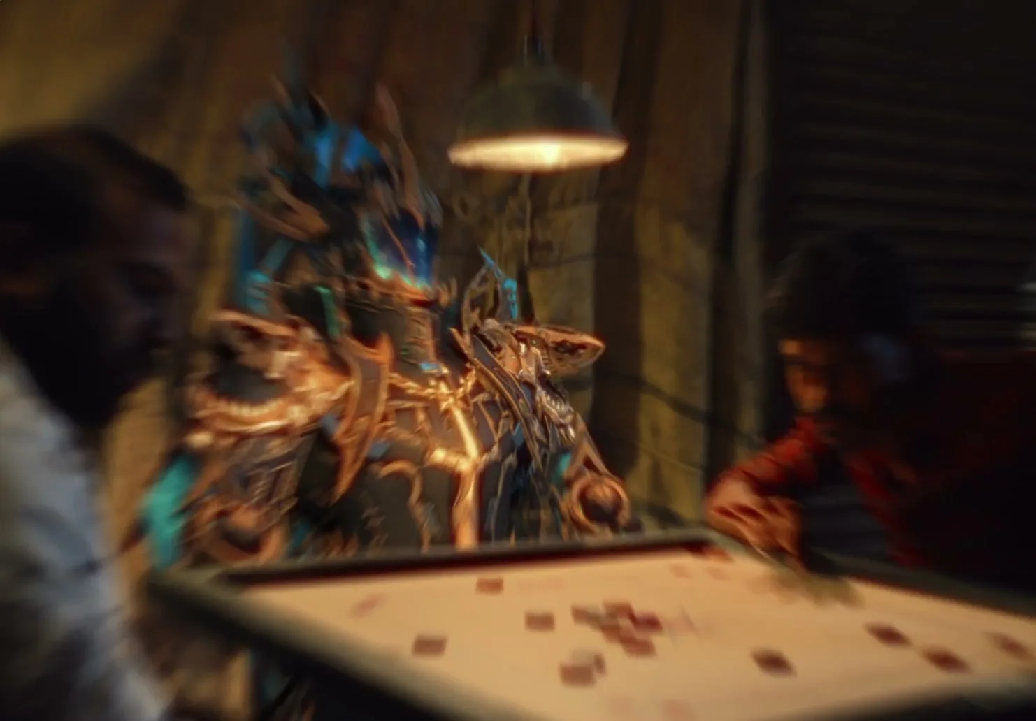 Three men play carrom in a dimly lit room, with one man replaced by a glowing, ornate CG warrior, as the camera moves around them.
