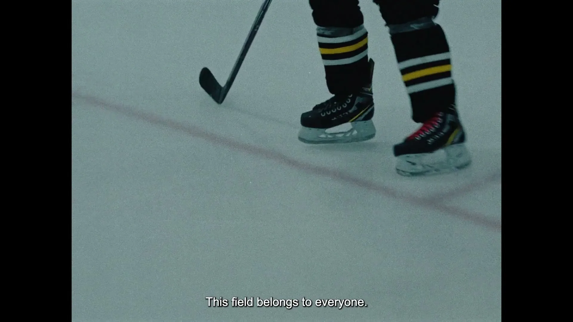 A person wearing black and yellow hockey gear and skates glides across an ice rink, holding a hockey stick.
