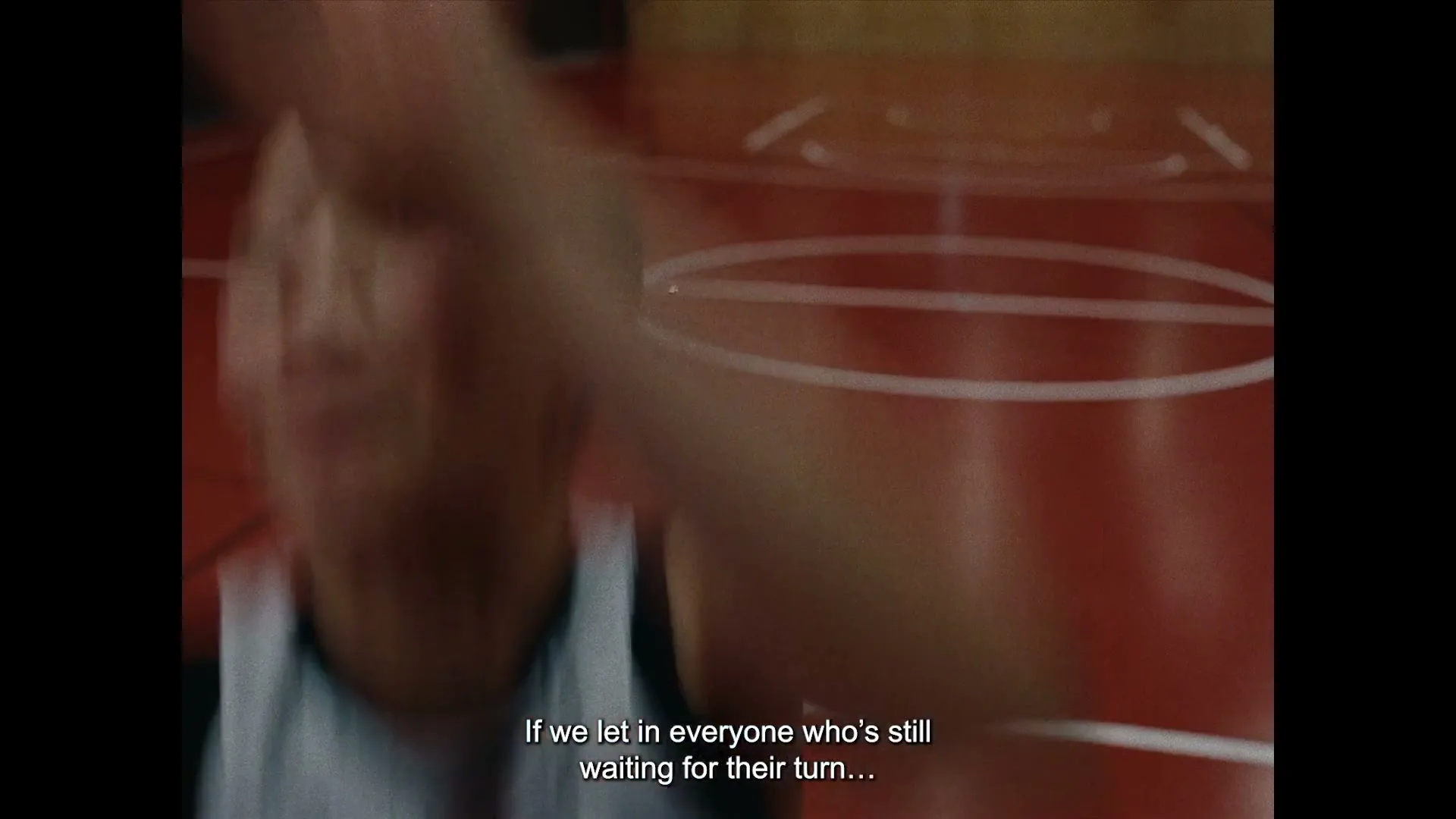 A person in a white and black jersey with a black bird graphic on the back runs across a red basketball court.