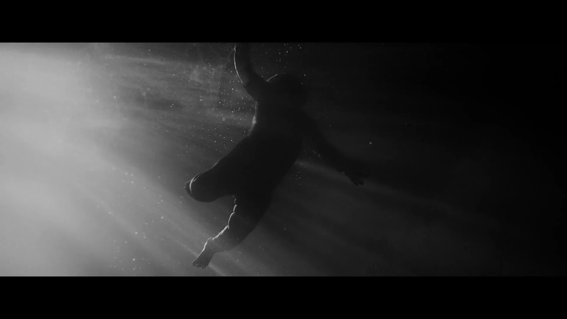 A baby, silhouetted against a bright light, floats in dark water, with light rays and particles visible.