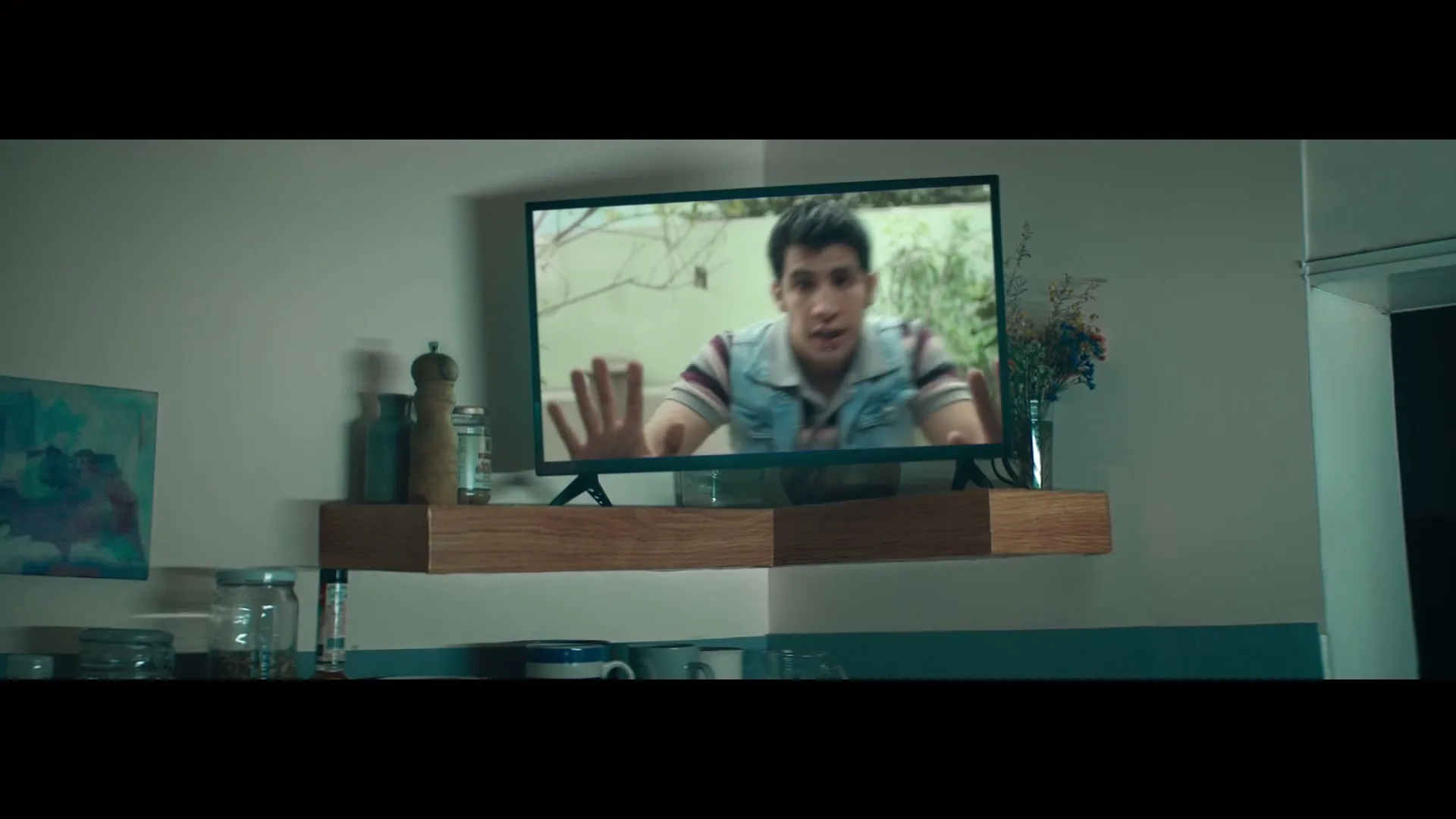 A young man on a TV screen reaches out with both hands, as if trying to escape the screen, in a kitchen.