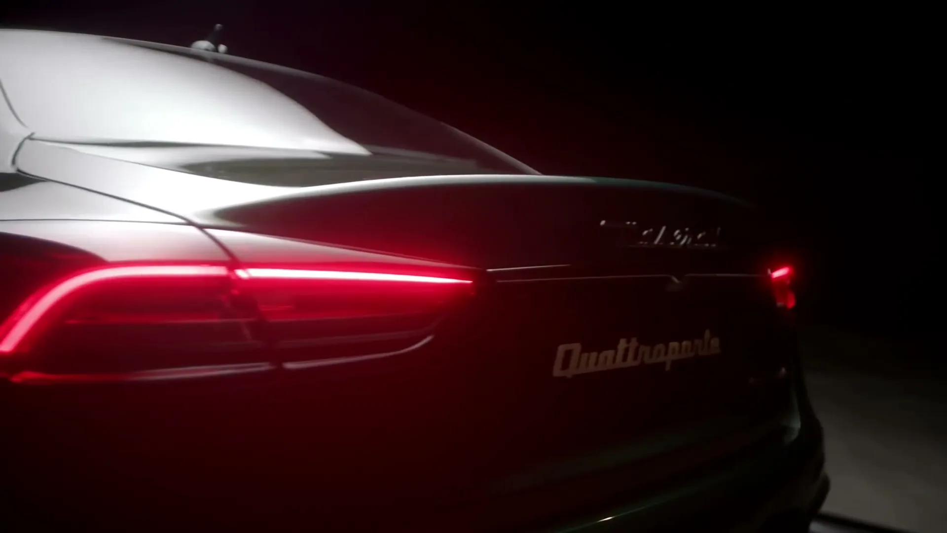 The rear of a dark Maserati Quattroporte with its red taillights illuminated is shown in a dark setting.