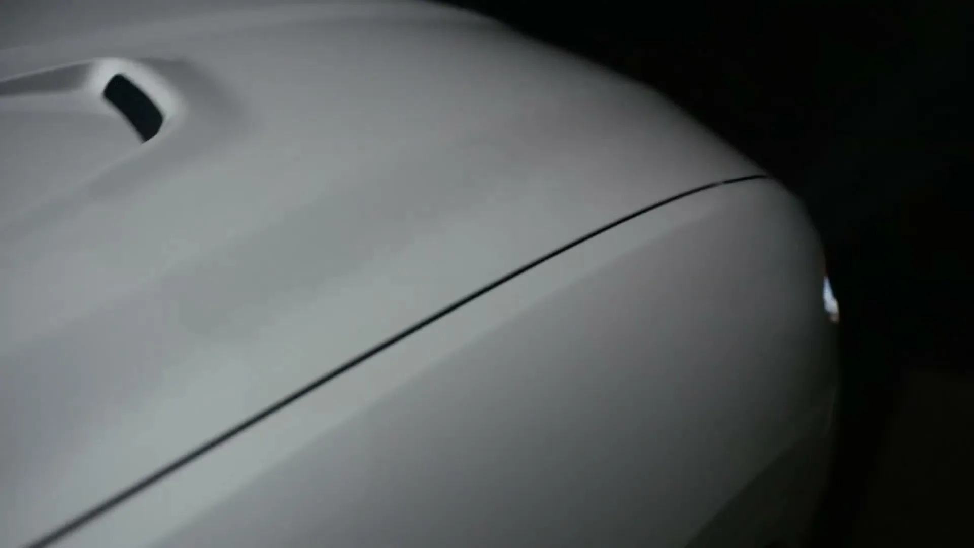 A white Maserati car is shown in a closeup shot, with its headlight turning on in a dark setting.