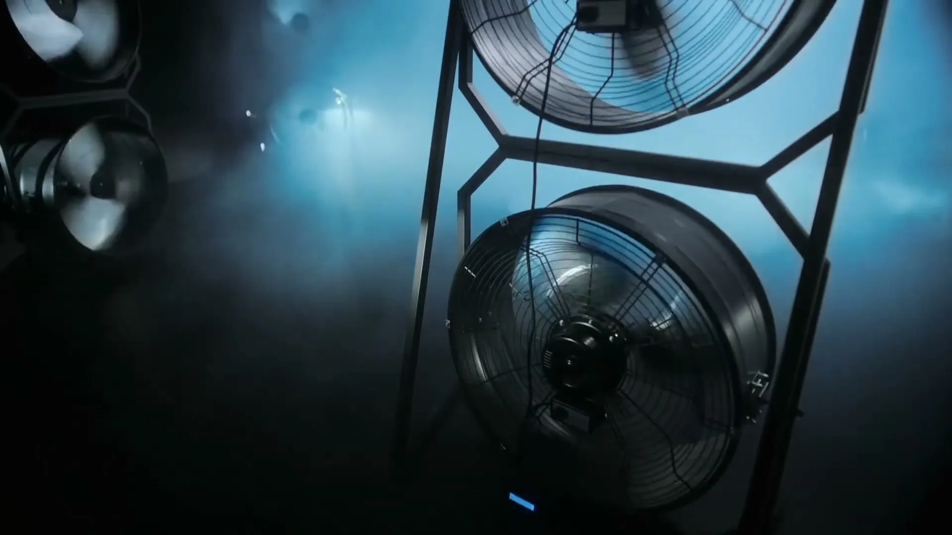 A close-up shot of large industrial fans blowing air in a dark, smoky room, creating a dramatic and powerful atmosphere.