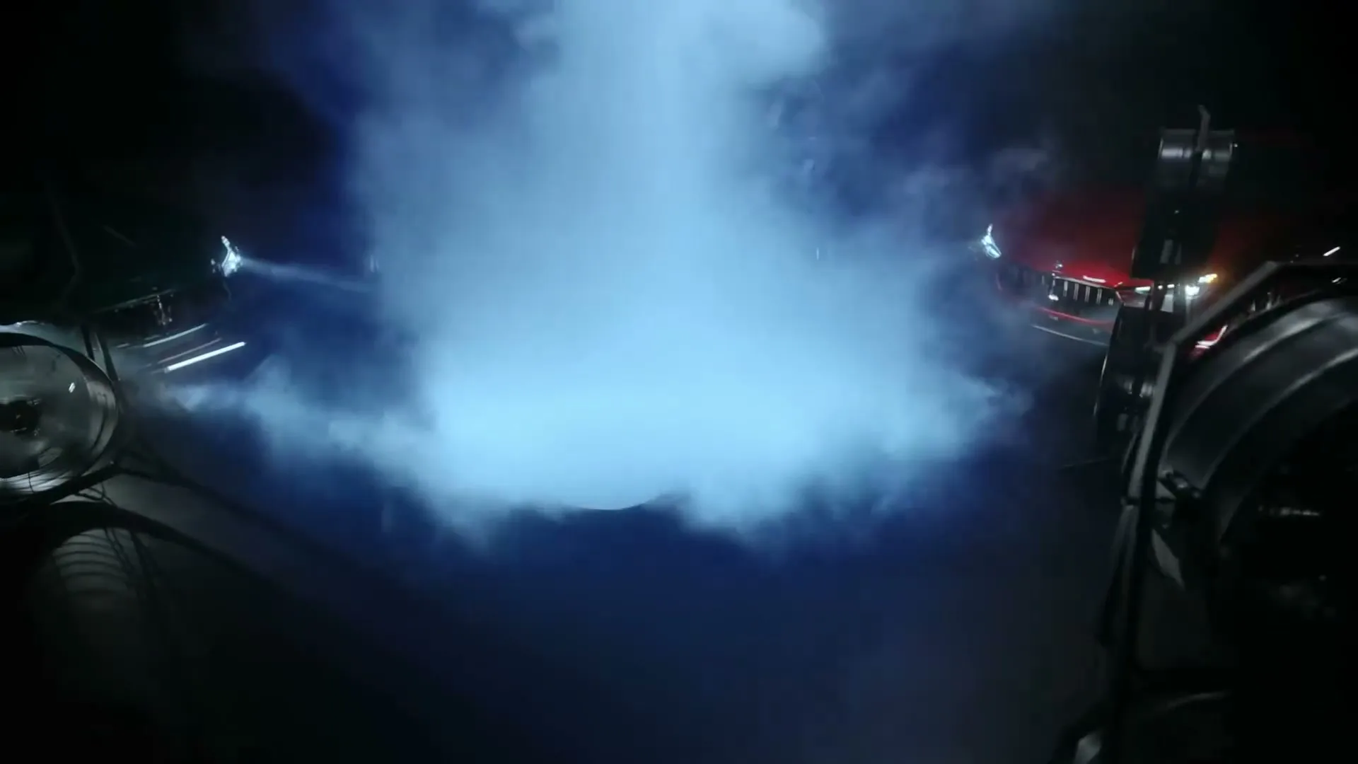 Two Maserati cars, one red and one green, are revealed from behind a cloud of blue smoke in a dark studio with large lights.