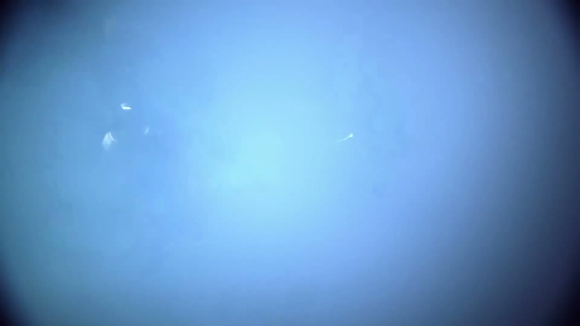A dark car with glowing headlights is partially visible through a thick cloud of blue smoke, with a large fan on the left.