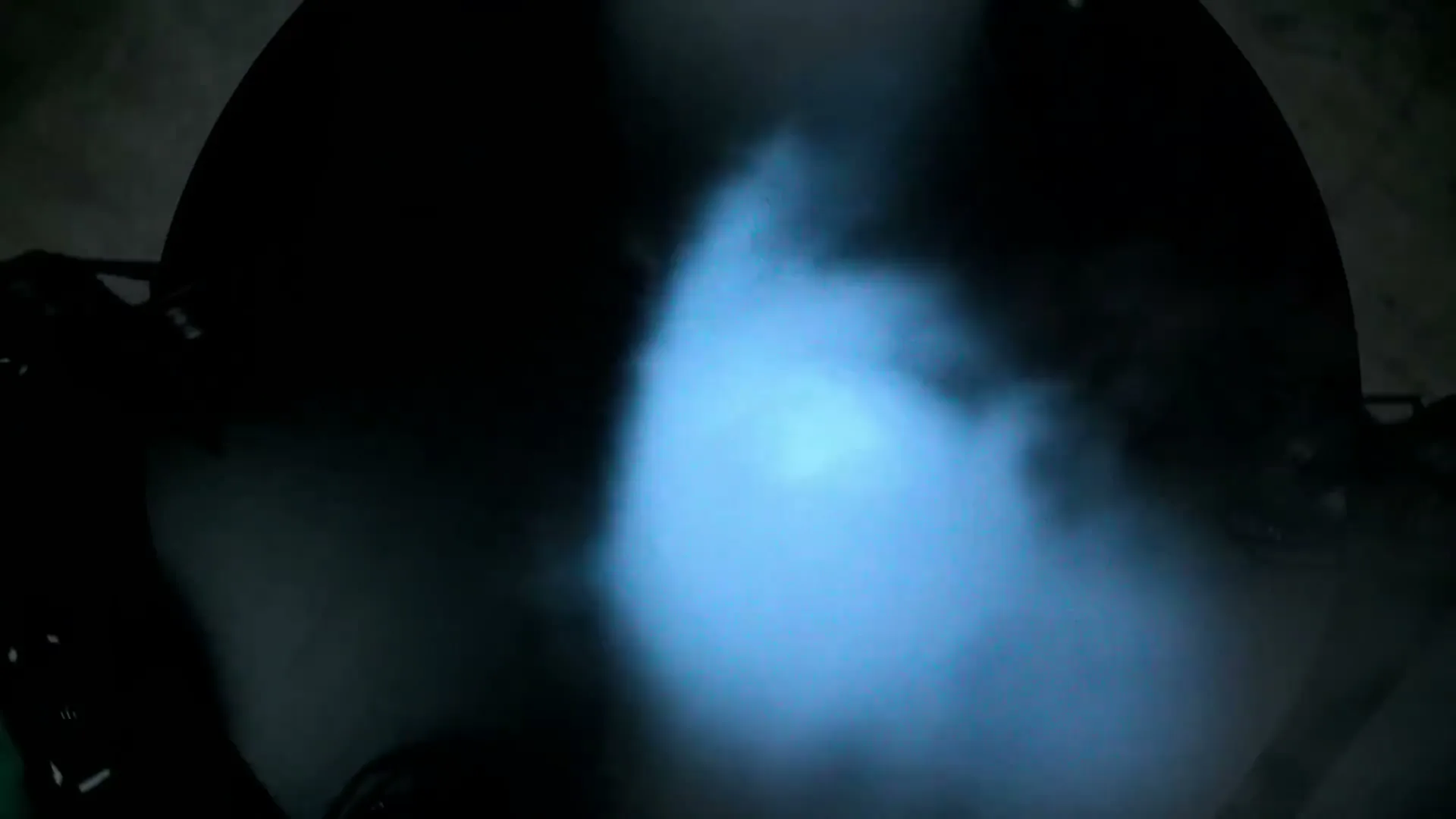 A blue light illuminates a dark, smoky tunnel as a vehicle speeds through, creating a dynamic and mysterious visual.