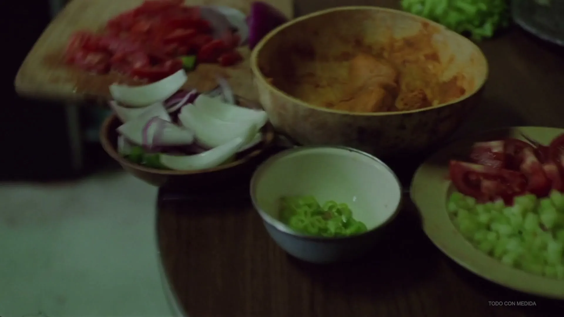 A close-up shot shows various chopped vegetables, including tomatoes, onions, and green peppers, arranged in bowls and on a cutting board on a wooden table.