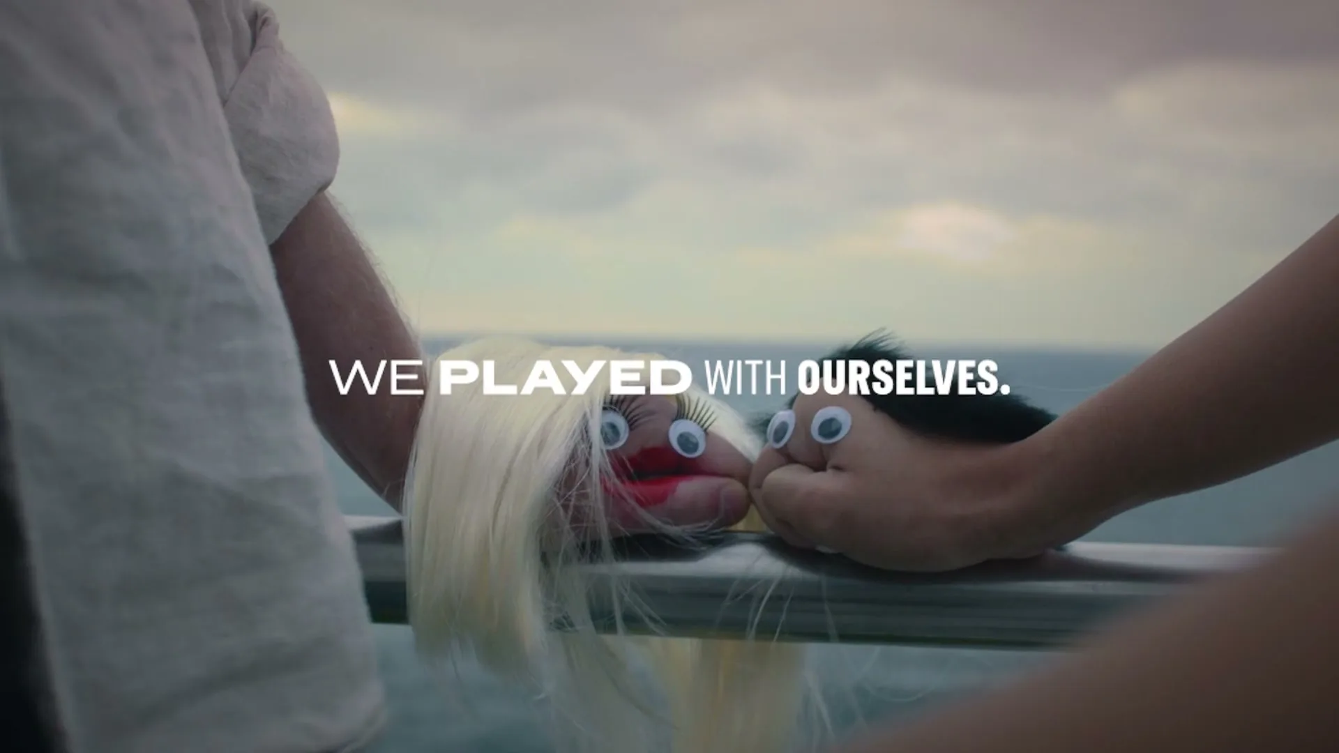 Two hands, dressed as puppets with googly eyes and hair, are shown on a railing with the ocean in the background, as text appears on screen.