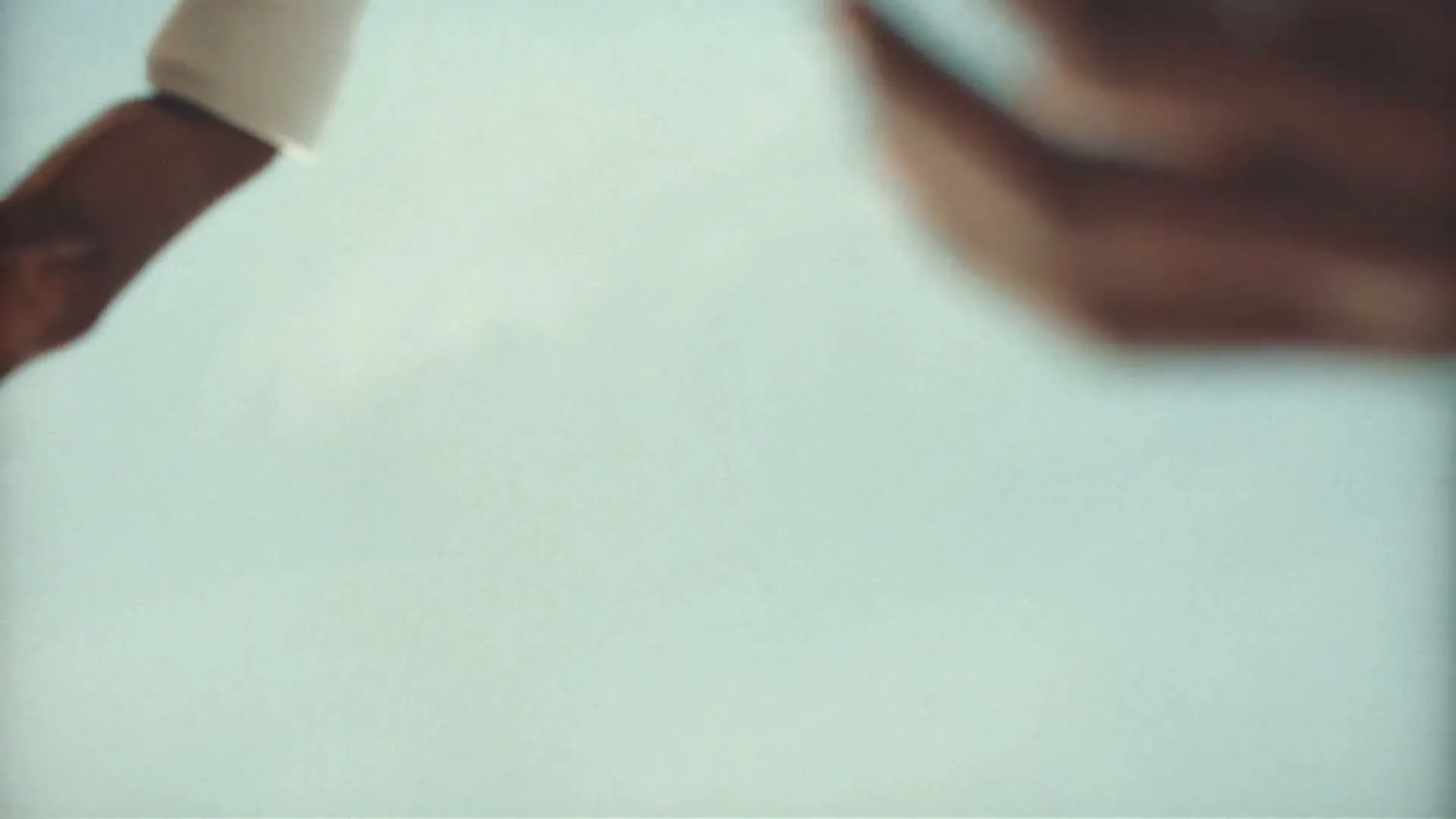 A person's arm and hand, wearing a white sleeve, reaches down into a light blue, hazy void.