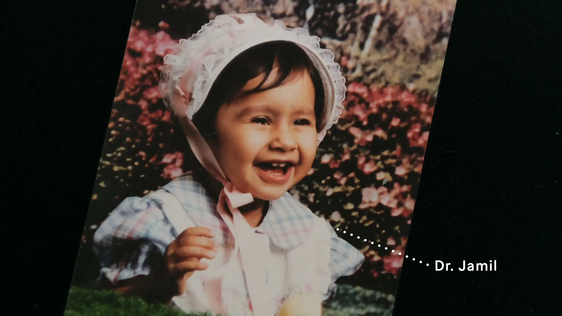 A close-up of a baby girl in a bonnet, laughing joyfully in a vintage photograph, with text "Dr. Jamil" appearing on screen.