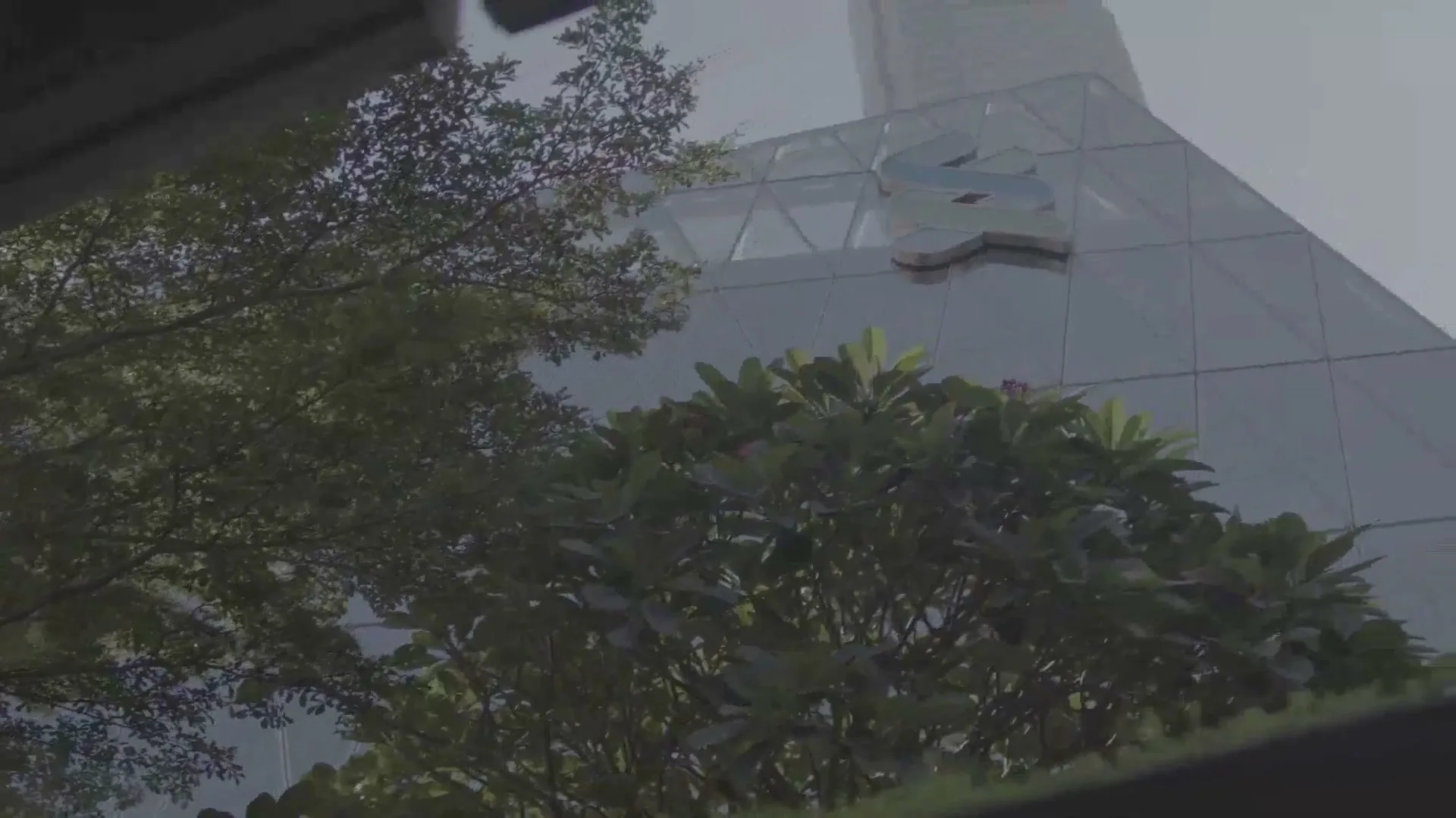 A low-angle shot captures the Standard Chartered logo on a modern glass building, partially obscured by lush green trees under a bright sky.