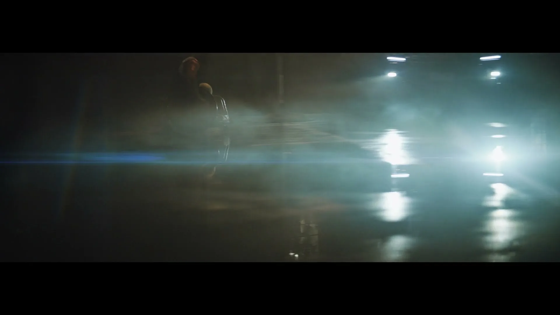 A dark, smoky scene with a person in the foreground and bright headlights of a car in the background, creating a strong lens flare.