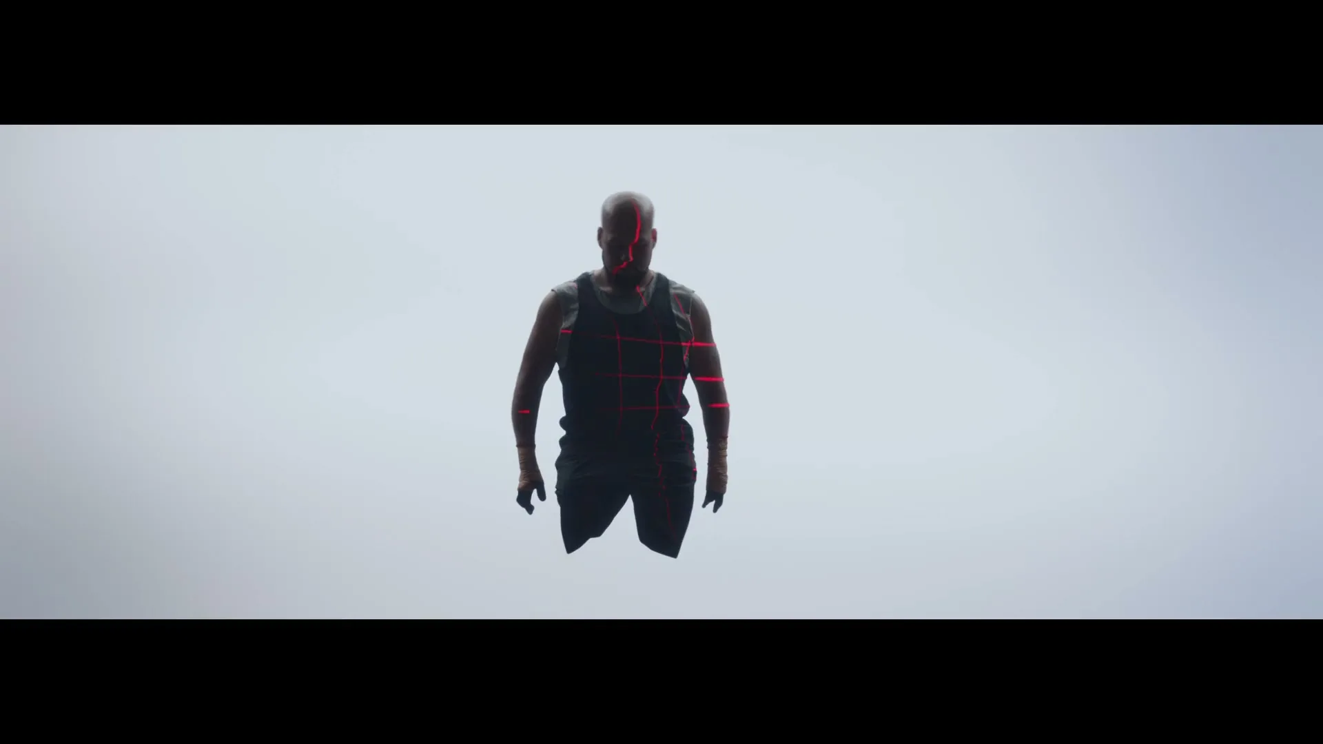 A bald man with red laser lines on his body floats in a white void, looking directly at the camera.